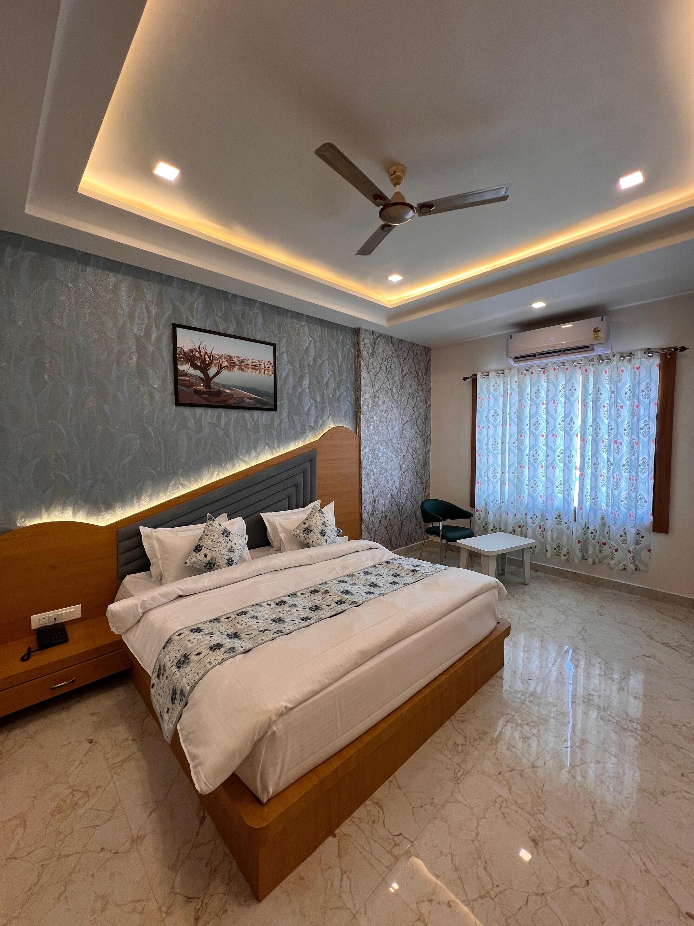 A modern bedroom with a large bed, a ceiling fan, recessed lighting, a wall-mounted air conditioner, and a window with patterned curtains.