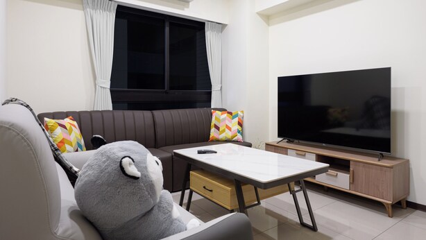A living room with a sofa, a TV, a coffee table, and a plush toy.