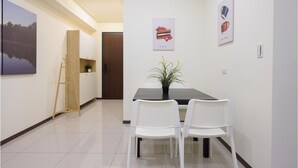 A dining area with a table, two chairs, a potted plant, and artwork on the walls.