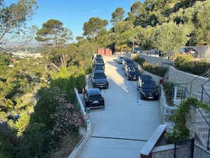 A parking area with cars parked along a road surrounded by trees and a stone wall.