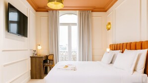 Ett hotellrum med en stor säng, en tv som är monterad på väggen, ett skrivbord med en lampa och utsikt över staden genom ett fönster.