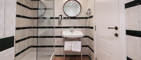 Une salle de bain avec une douche à parois de verre, un lavabo blanc avec un miroir au-dessus et une porte dotée d'une poignée.