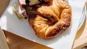 En croissant på en tallrik, tillsammans med en servett, ett glas marmelad och ett paket smör.
