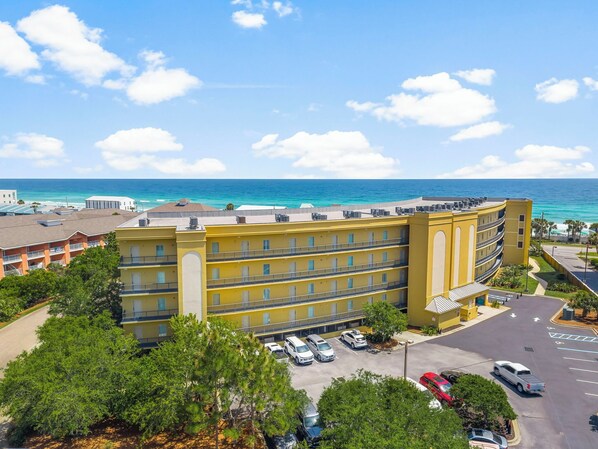 A multi-story hotel with a yellow facade, located near a beach with clear blue waters.