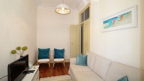 A living room with a white sofa, two wicker chairs with teal cushions, a TV, and a painting on the wall.