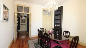 A dining area with a round table, six chairs, a chandelier, and a bookshelf.