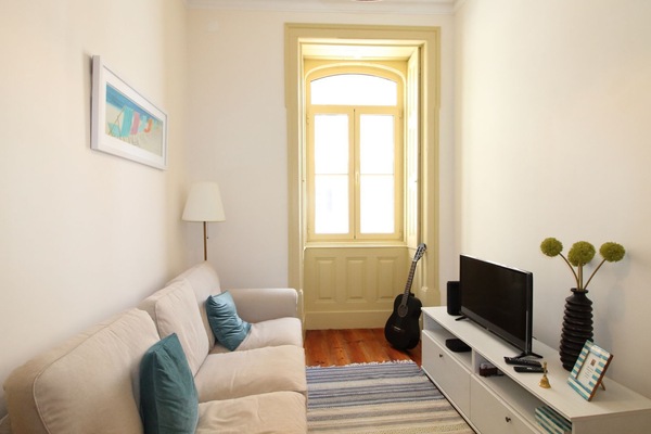 Relax in this charming and sunlit living room featuring classic Portuguese shutters, a plush beige sofa, and tasteful beach-themed artwork — the perfect nook for unwinding after a day in the city. #FigueiraApartment #CozyLiving #ShortTermRental