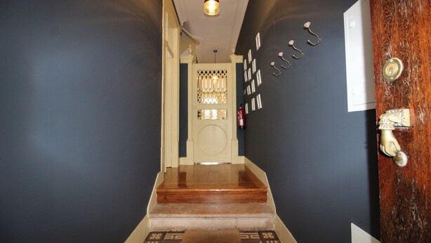 A narrow hallway with a wooden staircase leading to a door with a decorative glass panel.