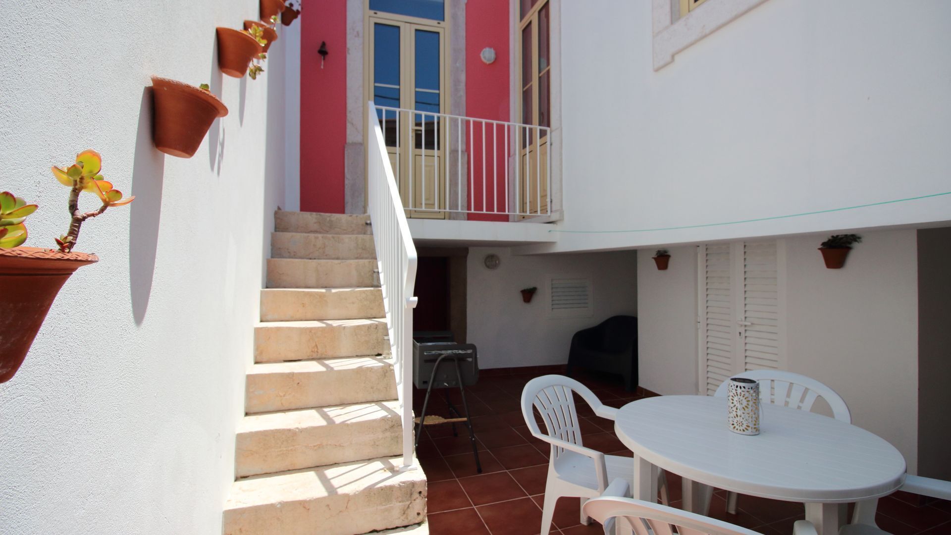 Une cour avec une table et des chaises blanches, un escalier et des plantes en pot.