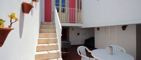 Une cour avec une table et des chaises blanches, un escalier et des plantes en pot.