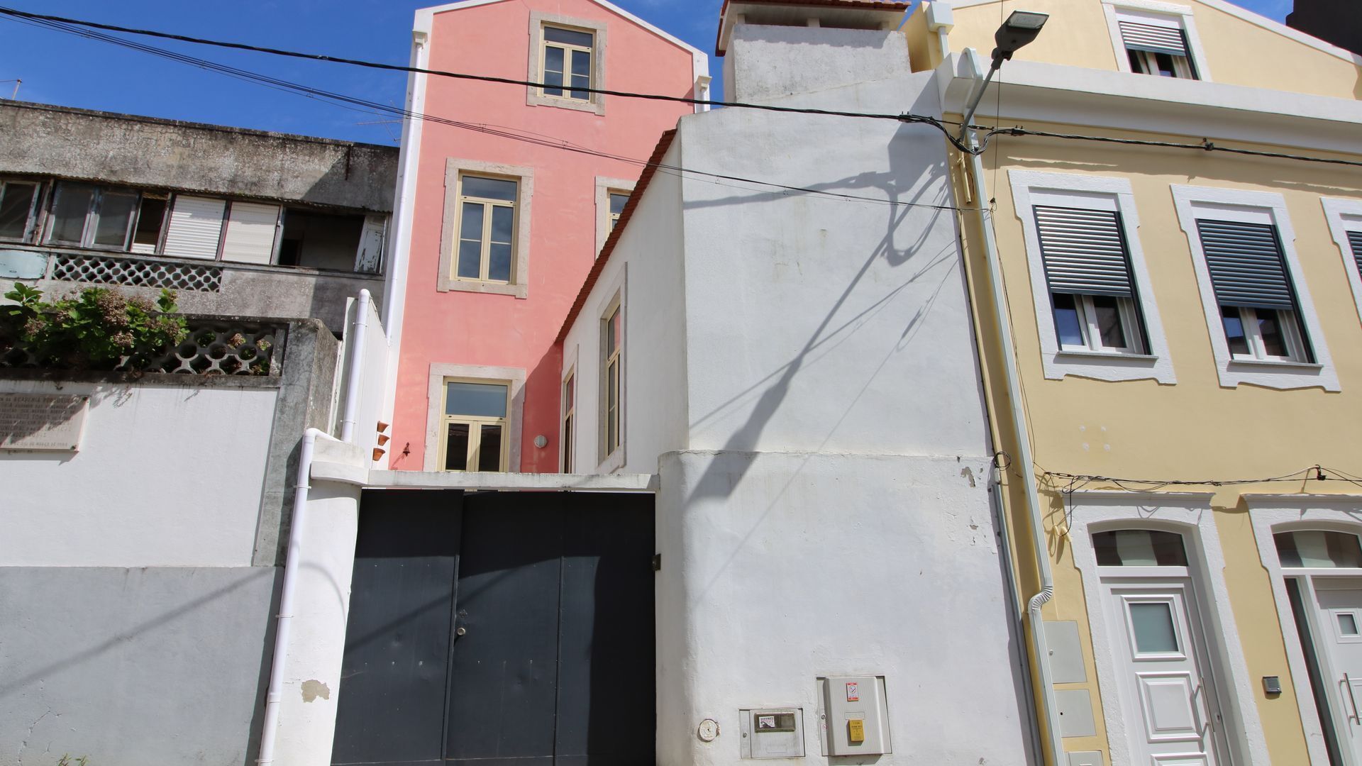 A multi-story building with a pink and white facade, a black garage door, and a yellow building with shutters.