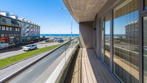 Ein modernes Gebäude mit großen Fenstern, das auf eine belebte Straße und das Meer blickt.