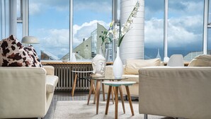 Una sala de estar moderna con vistas a un edificio y al cielo a través de grandes ventanales.