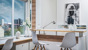 Una cocina moderna con encimera de madera, sillas blancas, un florero con flores y vistas a la ciudad a través de amplios ventanales.