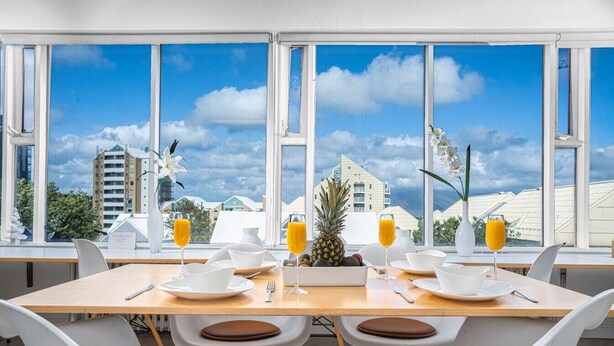 Una mesa con sillas dispuesta para el desayuno, con vistas a edificios a través de amplias ventanas.