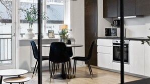A modern kitchen with white cabinets, a black countertop, and a microwave. There is a dining area with a table and chairs, and a window with a view of the outside. - Central and Cozy Apartment (Reykjavík)