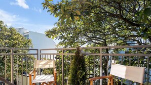A balcony with two wooden chairs, a woven basket, and a view of trees and buildings. - Central and Cozy Apartment (Reykjavík)