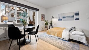 A modern bedroom with a bed, a desk with chairs, and a window with a view of trees and a building. - Central and Cozy Apartment (Reykjavík)