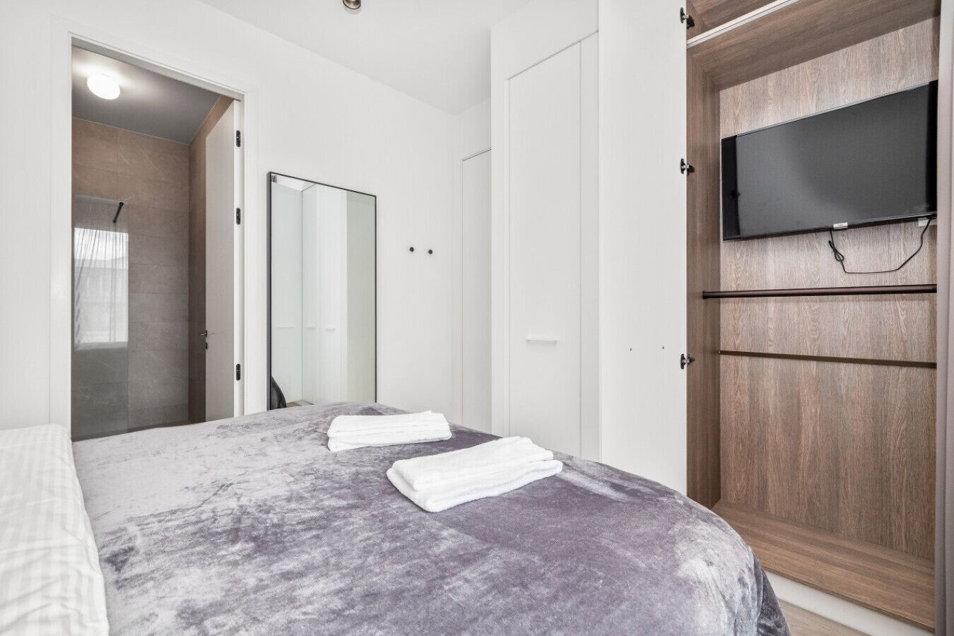 Ein Schlafzimmer mit einem Bett, einem an der Wand befestigten Fernseher und einem Holzschrank.