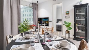 A modern dining area with a round table set for six, a television in the background, and a bookshelf with decorative items. - Vibrant City Center Escape (Reykjavík)