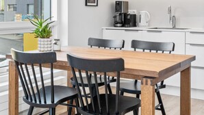 Una cocina moderna con armarios blancos, una mesa de comedor de madera y sillas negras. Una lámpara colgante ilumina la mesa.