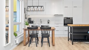Una cocina moderna con armarios blancos, una mesa de comedor de madera con cuatro sillas y una lámpara colgante.