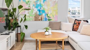 Una sala de estar moderna con una mesa de centro redonda de madera, un sofá blanco y un cuadro abstracto grande en la pared.
