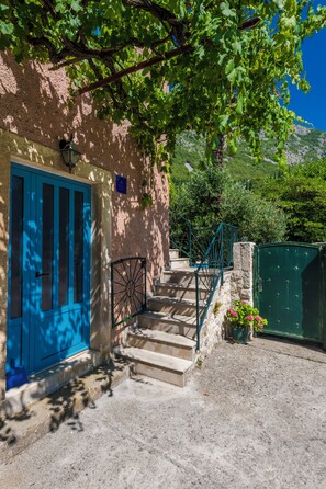 A stone building with a blue door and a staircase leading to a gate.