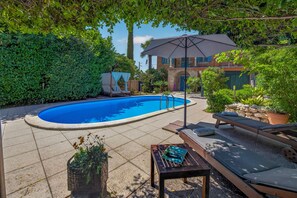 Una piscina amb un parasol, gandules i una taula petita amb una tovallola.