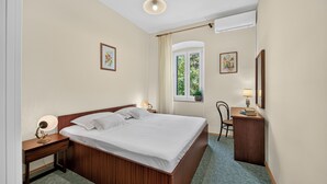 Ein Hotelzimmer mit einem großen Bett, Nachttischen, einem Sessel, einem Schreibtisch und einem fenster mit Vorhängen.