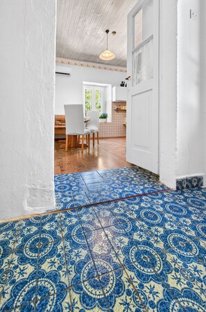 Une pièce avec un sol à motifs bleus et blancs, une table à manger en bois avec des chaises, et une porte blanche.