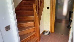 A wooden staircase with a handrail, a door with a metal handle, and a pair of shoes on the floor.