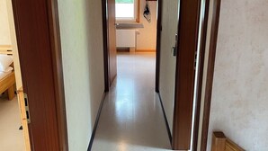 A narrow hallway with wooden doors on either side, leading to a room with a window and a radiator.