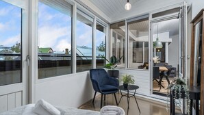 Ein modernes Schlafzimmer mit einem großen Bett, einem blauen Sessel, einem kleinen Tisch und Blick auf die Stadt durch große Fenster.