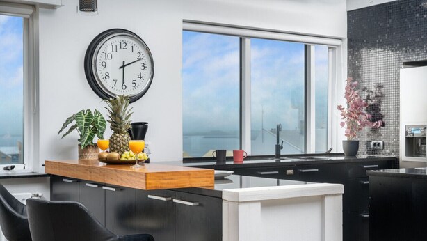 Eine moderne Küche mit einer Holzinsel, schwarzen Schränken, einer großen Uhr und Blick aufs Meer.