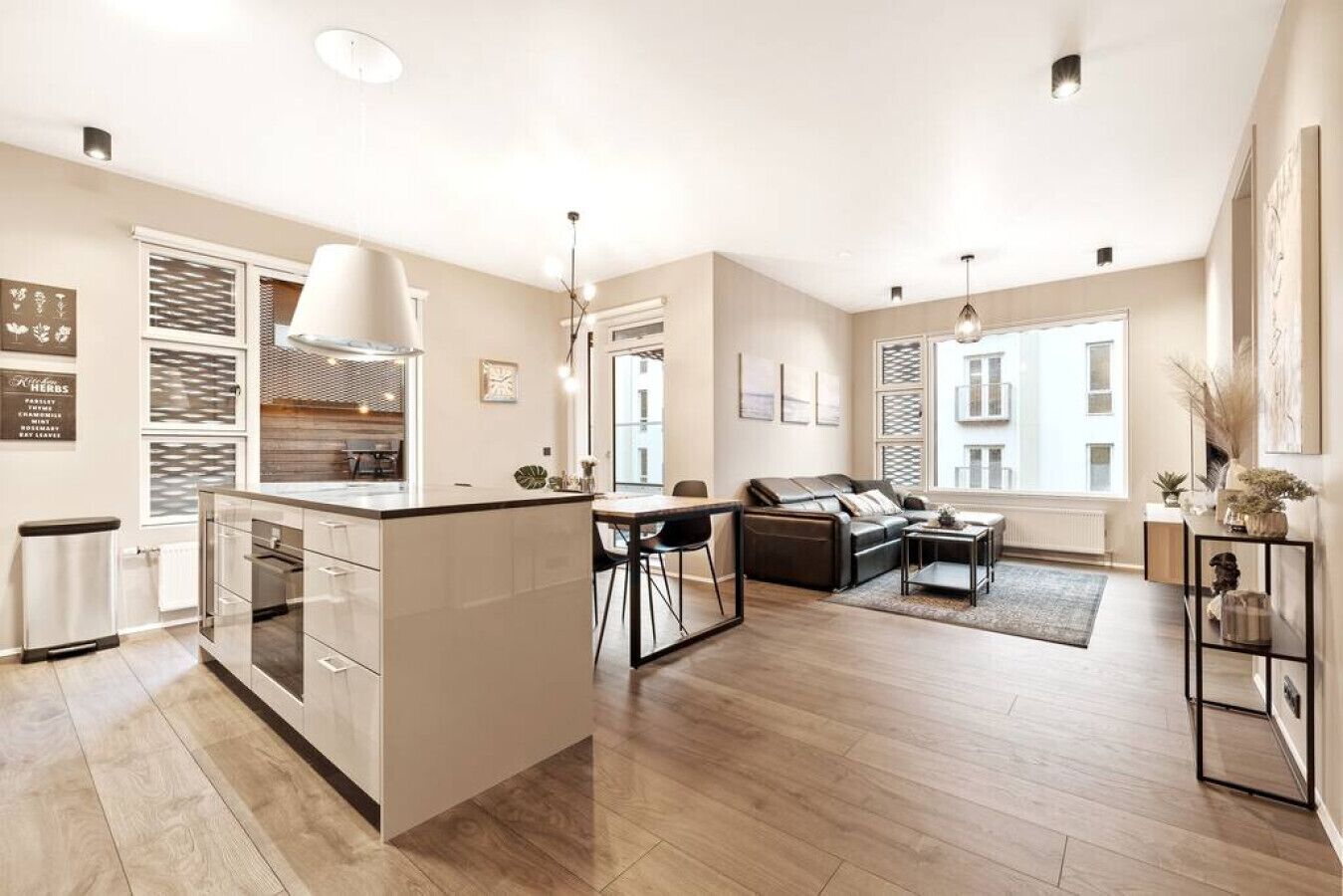 A modern kitchen with a central island, a dining area with a sofa, and a living room with a large window.