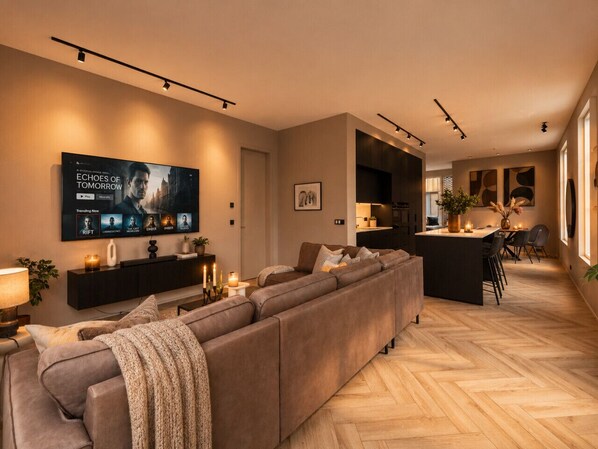 Ein modernes Wohnzimmer mit großem Flachbildfernseher, einer Couch, einem Essbereich mit Bar und einer Küche im Hintergrund.