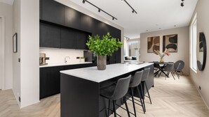 Une cuisine moderne avec des meubles de couleur sombre, un îlot central doté de tabourets de bar et une grande fenêtre qui laisse entrer la lumière naturelle.