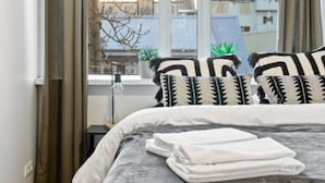 A bedroom with a large bed, a window with curtains, and a view of buildings outside. - Prime Location Gem in the Heart of Reykjavík (Reykjavík)