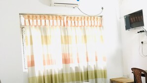 Una camera da letto con un letto, un ventilatore a soffitto, un condizionatore, una TV e una finestra con tende.
