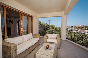 A balcony with wicker furniture, a table with a candle, and a view of buildings and trees. - Zen Maisonette Retreat (Chania)