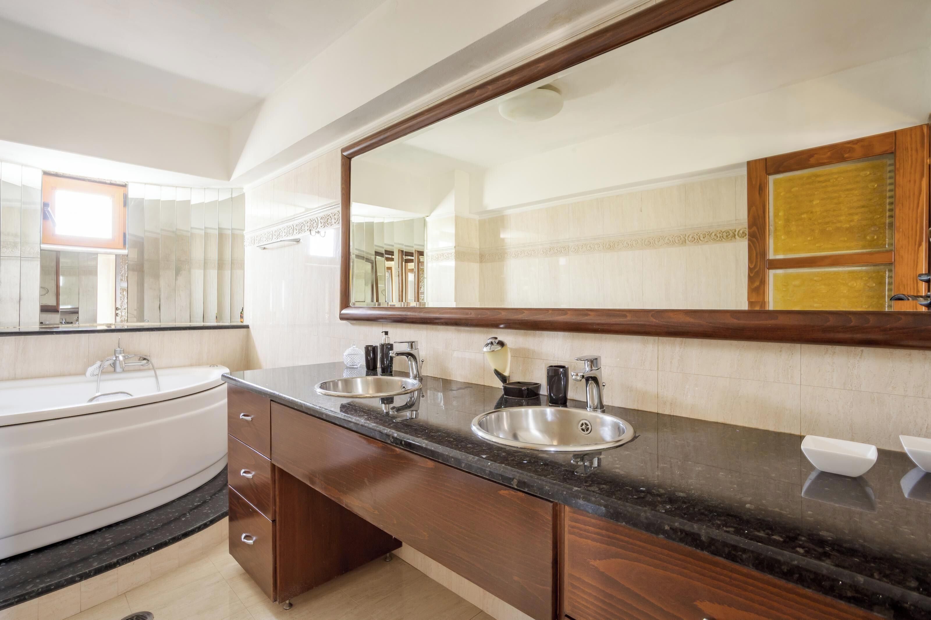 A modern bathroom with two sinks, a large mirror, and a bathtub.