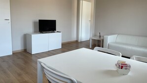 Una sala de estar moderna y minimalista con un sofá blanco, un mueble blanco para televisión y una pequeña mesa blanca.