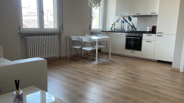 Una cocina moderna con armarios blancos, un comedor con mesa y sillas, y un radiador.