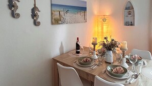 A dining area with a wooden table set for two, featuring a candle, a bottle of wine, and a vase with flowers. - Lines to Huus Vacation Home – Near the Baltic Sea Beach (Neukirchen)