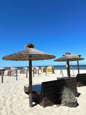 A beach with wooden lounge chairs and thatched umbrellas, a sandy beach, and a clear blue sky. - Lines to Huus Vacation Homes & Apartments – Heiligenhafen, Near the Beach, Baltic Sea & Dog-Friendly (Neukirchen)