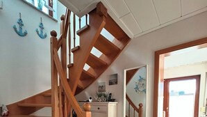 A wooden staircase with a white wall and a small cabinet below. There is a mirror reflecting the staircase and a door leading outside. - Lines to Huus Vacation Home – Near the Baltic Sea Beach (Neukirchen)