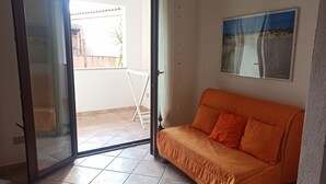 A room with a sliding glass door leading to a balcony, a single orange sofa, and a framed picture on the wall.