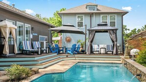 Un jardin avec une piscine, des chaises Adirondack bleues, un patio couvert et une maison à la façade bleu clair.