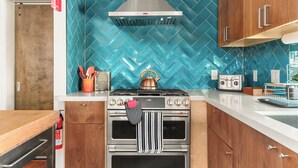 Une cuisine dotée d’une cuisinière en acier inoxydable, de meubles en bois et d’un dosseret de carrelage disposé en motif chevrons.